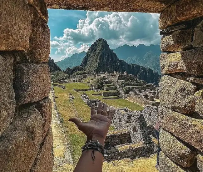 Machu Picchu Viewpoint | Conde Travel Adventures Hand pointing at Machu Picchu ruins framed by stone walls | Conde Travel Adventures